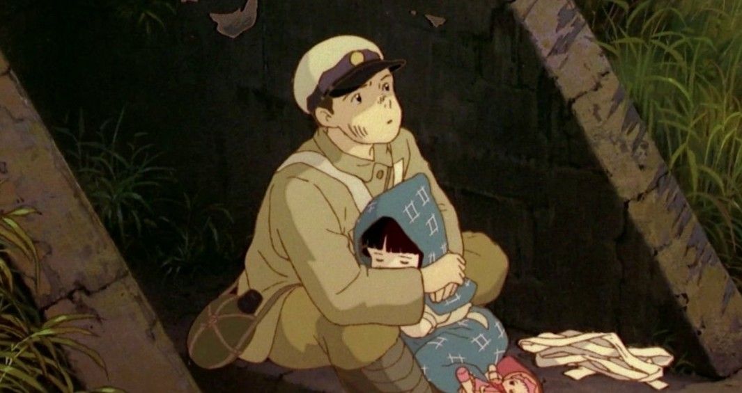A sad scene from Grave of the Fireflies, showing Seita in a soldier's uniform holding his sleeping little sister.