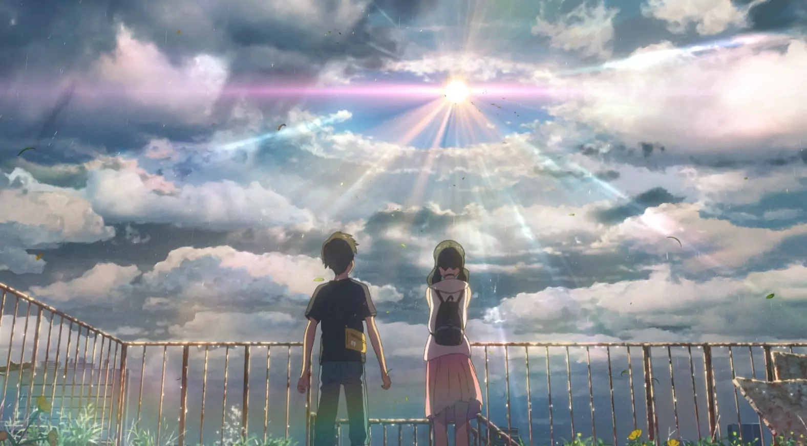 Hodaka and Hina watching a dramatic sky filled with sunbeams and a rainbow from a rooftop in the anime movie Weathering With You.